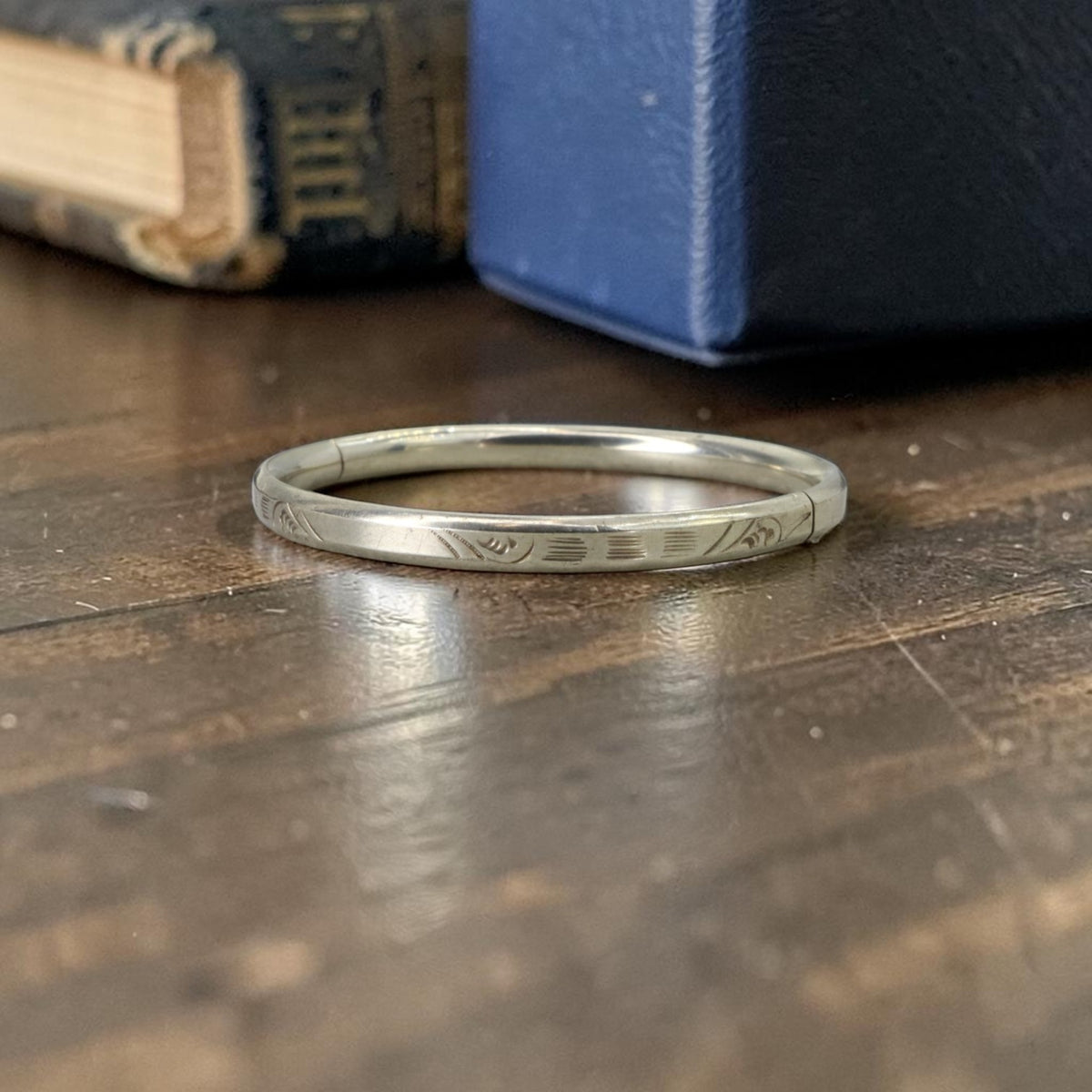 1920s Art Deco hand engraved bangle bracelet in white gold shell resting on a wood surface