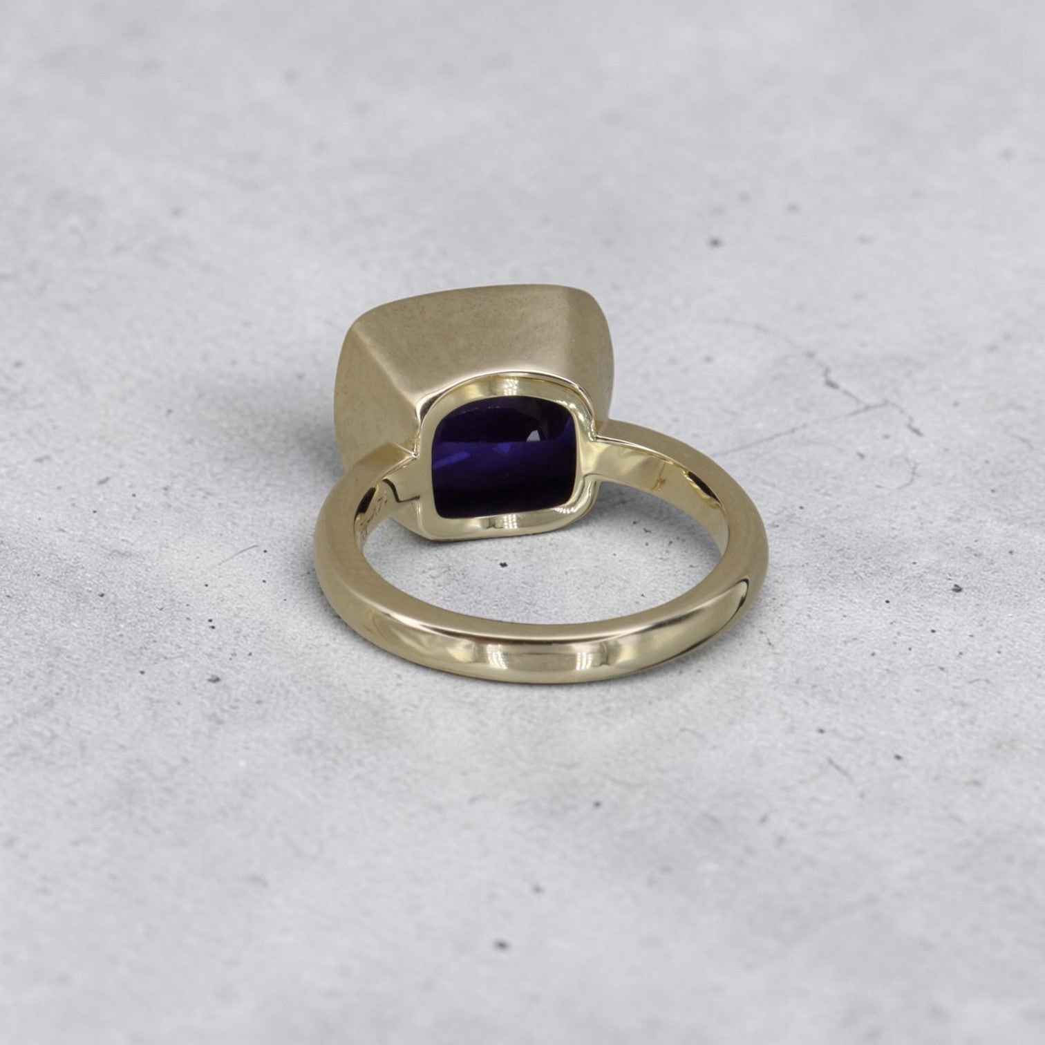 Cushion-cut tanzanite ring in 14k yellow gold with custom mounting, featuring a vibrant blue-purple gemstone and elegant band design.
