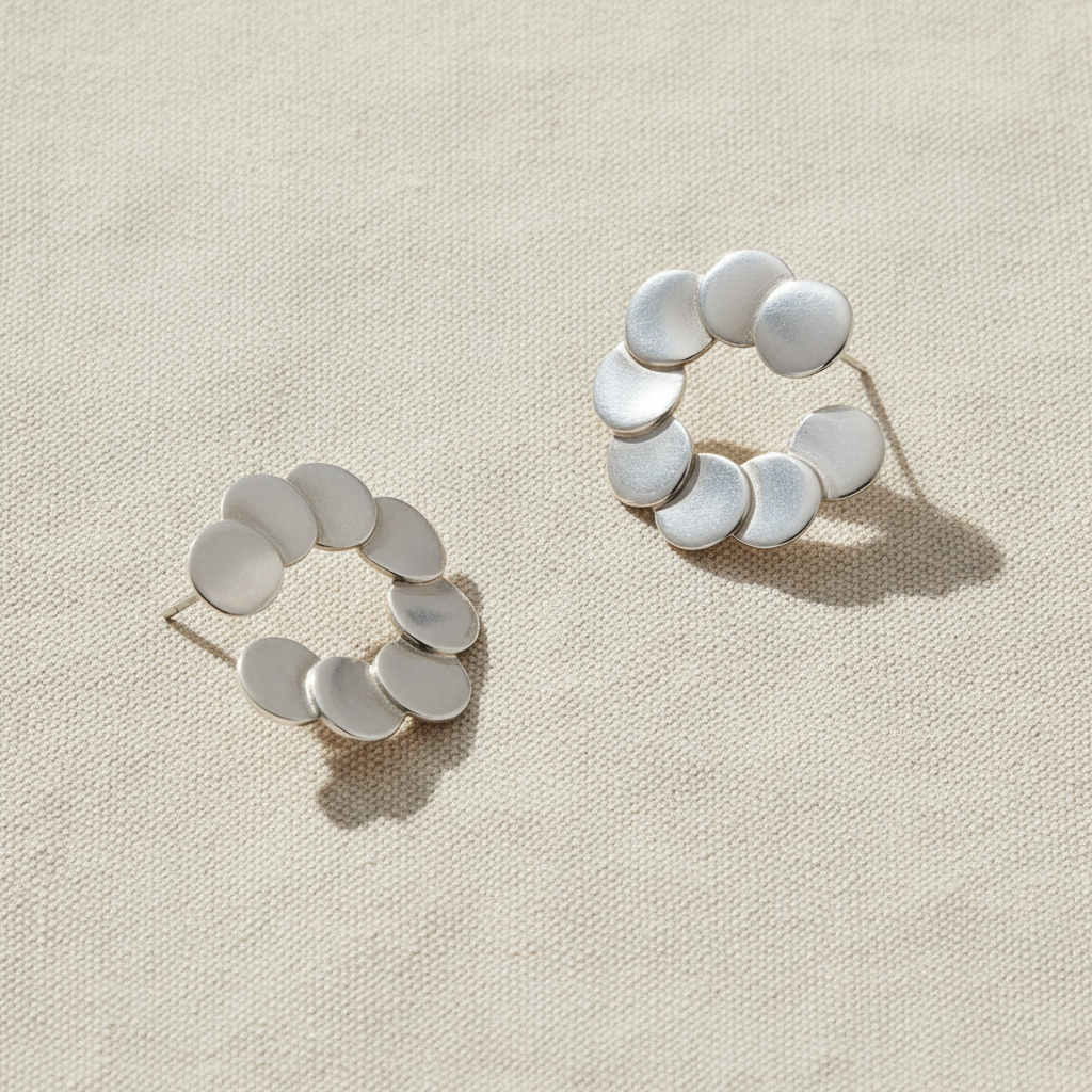 A pair of silver huggie hoop earrings with a textured, overlapping disc design, shown on a clean white background.