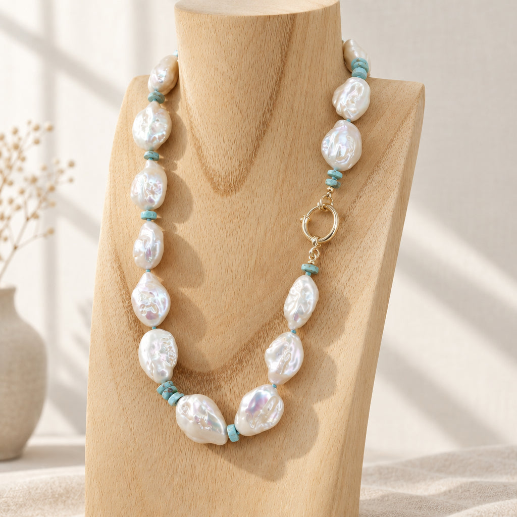 A beaded necklace with irregular white baroque pearls and small turquoise-blue spacer beads, displayed on a light wood neck stand.