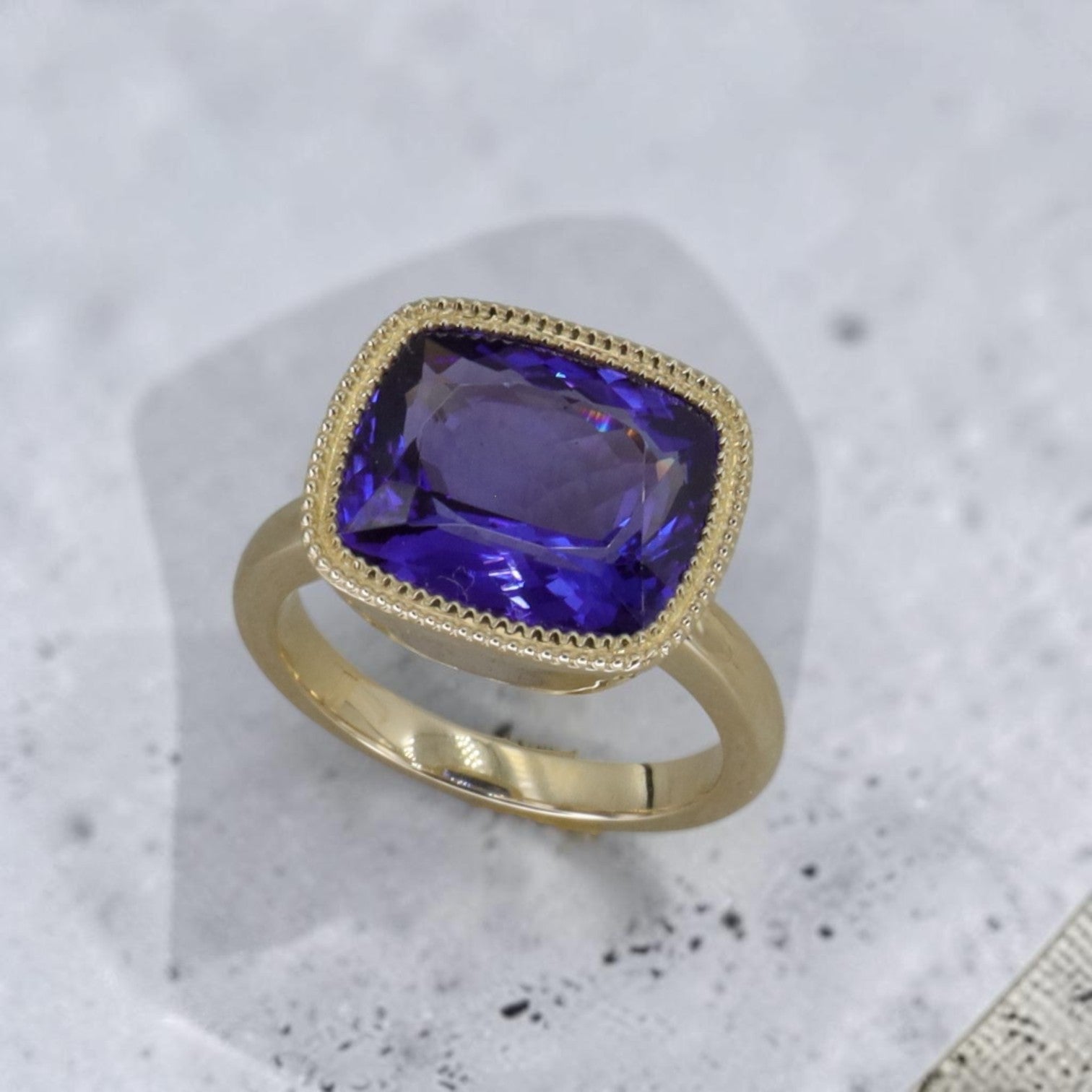 Bezel-set cushion-cut Tanzanite ring in 14k yellow gold by Petra Star, showcasing the vibrant blue gemstone on a polished band.