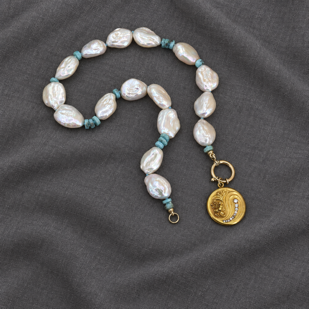 White keshi pearl and blue larimar necklace with an open gold-tone charm-holder clasp and coin charm on charcoal linen.