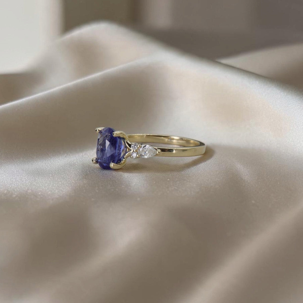 Angled view of oval sapphire ring with pear-shaped diamond side stones in 14k yellow gold