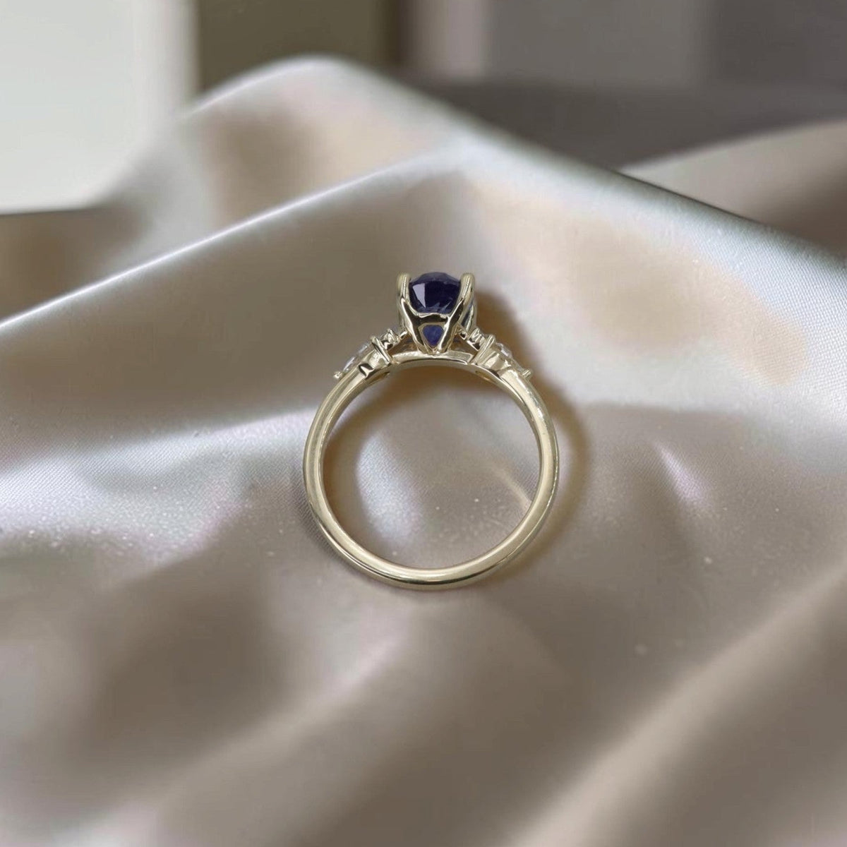 Through-finger view of oval sapphire ring with diamond shoulders on a 14k yellow gold band